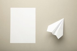 Flat lay of white paper plane and blank paper on grey background. Top view