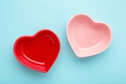Red and pink heart shaped bowls on blue background. Top view
