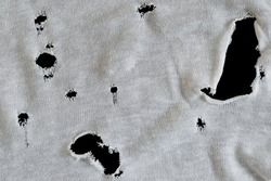 Gray white fabric with many holes. Texture of an old dirty ragged t shirt. Grunge damaged cloth on black background. Crumpled torn rag. Copy space