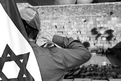 Israeli soldier with Flag of Israel salutes on the blurred background of Western Wall in the Old City of Jerusalem in Israel