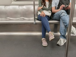 young couple (boy and girl friends) sit in spacious public subway train in Hong Kong, China, man playing mobile phone