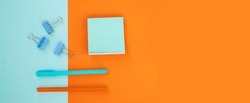 Minimum set of school and office supplies on bright blue (turquoise) and orange background: pen, clips, note paper. Concept: back to school. Flatlay, top view.