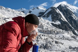 High altitude sickness. Climber breathing oxygen from the O2 tank on the background of glacier and covered with snow and ice mountains.