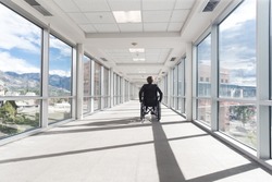Solitary middle aged woman in a wheelchair in a hallway of a medical center or other building on a sunny day