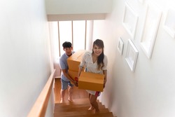happy woman and man moving in new home. asian adult couple move carton box relocating into new house for bonding relationship. beautiful girlfriend and handsome boyfriend change new place to be home.