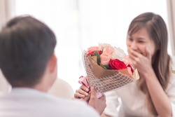 handsome husband giving flowers to beautiful wife. cute surprised girlfriend got present from happy boyfriend. adult couple with good comfortable relationship give lovely flowers for romantic touch.