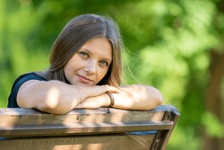 Portrait of a beautiful girl sitting on a bench and looking happily into the frame