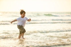 Portrait Happy little Asian boy running and playing with smiling and laughing on tropical beach at sunset. Portrait of Adorable young child kids having fun in summer holiday vacation travel.