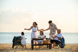 Happy Asian family on holiday vacation. Group of multi generation family little girl with parents and grandparents relax and enjoy with dinner party and dancing together on the beach at summer sunset.