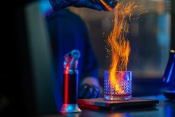 Asian man bartender making special cocktail explode alcoholic drink with cinnamon powder on bar counter serving to customer at nightclub with neon night lights. Small business food and drink concept