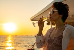 Confident Caucasian woman relax and enjoy luxury outdoor lifestyle drinking champagne while travel on catamaran boat yacht sailing in the ocean at sunset on summer beach holiday vacation trip