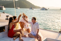 Group of Man and woman friends enjoy and fun luxury outdoor lifestyle celebration party drinking champagne together while travel on catamaran boat yacht sailing in the sea at sunset on summer vacation