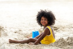 Little cute African child girl sitting on tropical beach playing sand and beach toy with smiling on summer vacation. Happy children kid enjoy and fun outdoor activity lifestyle on beach holiday travel