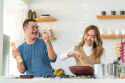 Group of Smiling Asian people friends enjoy cooking with talking together in the kitchen at home. Happy man and woman having dinner party meeting celebration eating food together on holiday vacation