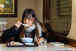 Young Asian woman tourist eating Japanese food breakfast rice ball with soup at local Japanese restaurant in snow day. Attractive girl enjoy travel small town in Japan on winter holiday vacation.