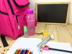Multi colored pencils, glue, ruler, eraser. pencils, book, bag, scissors and black board on a wooden table background. Education, Examination or Back to School concept.