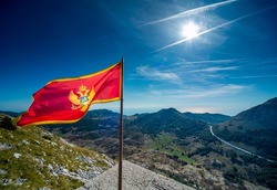 At the summit of Lovcen mountain,the majestic red national flag of the balkan state flapping in the wind,against clear,blue sunny skies of late summer.