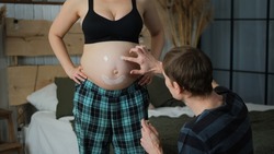 Male Drawing Funny Smiley Face on Belly of his Pregnant Wife at Home. Family Preparing for Newborn
