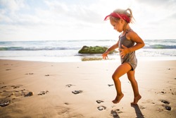 little adorable girl 2-3 years plays joyfully on the beach in sunset  on holiday