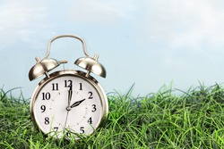 Set your clocks back with this clock in grass against a bright sky. Daylight saving time concept background.
