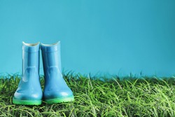 Blue children's rain boots / wellies sitting in the grasss agaisnt a blue background with room for copy space. 