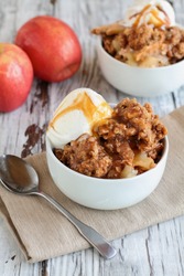 Fresh hot homemade apple crisp or crumble with crunchy streusel topping topped with vanilla bean ice cream and Caramel Sauce. Selective focus with blurred background. 