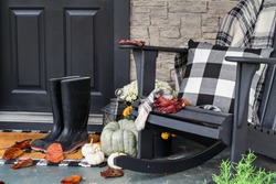Traditional style front porch decorated for autumn with rain boots, heirloom gourds,  white pumpkins, mums and rocking chair with buffalo plaid pillow and throw blanket giving an inviting atmosphere.