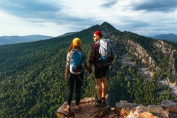 A traveling couple in hiking gear in the mountains at sunset. Two tourists on the top of the mountain. A man and a woman in the mountains. Hiking in the mountains with backpacks. Two travelers
