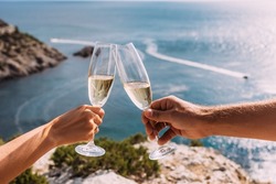 Hands holding champagne glasses over the sea. Romantic vacation. Two hands holding champagne glasses on the background of the sea. A couple in love drinks champagne on the seashore. Copy space