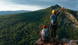 A traveling couple in hiking gear in the mountains at sunset. Two tourists on the top of the mountain. A man and a woman in the mountains. Hiking in the mountains with backpacks. Two travelers