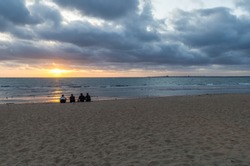 Sunset at St Kilda beach in Melbourne, Australia, with four unidentifiable people silhouetted against the light, sitting on the beach.