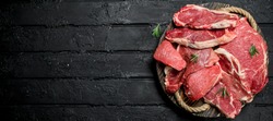 Raw meat. Beef and pork steaks on a wooden tray. On a black rustic background.