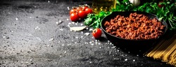Bolognese sauce in a frying pan with pasta dry and parsley. On a black background. High quality photo