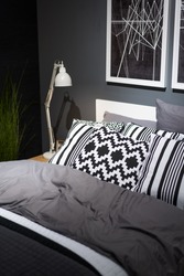 Bed with pillows in the bedroom near black wall. Interior in black and white colors