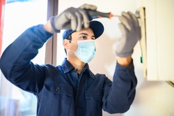Smiling technician repairing an hot-water heater wearing a mask due to coronavirus pandemic