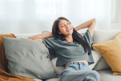 Relaxed young asian woman enjoying rest on comfortable sofa at home, calm attractive girl relaxing and breathing fresh air in home, copy space.