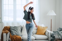 Happy carefree asian woman wearing headphones have fun moving listening to music relax in living room, She dance enjoy leisure weekend at home.