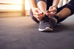 Woman tying running shoes on black floor background in gym. copy space.