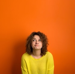 Cute model in yellow sweater among orange background with funny face. Thinking and wondering concepts. Lots of copy space for advertising