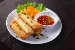 Fried spring rolls on a white plate and spicy sauce