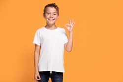 Young emotional handsome boy standing on orange studio background. Human emotions, facial expression concept.