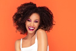 Happy smiling woman with glamour makeup. Photo of young african woman on orange background.