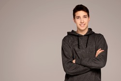 Portrait of a handsome teenage boy in hoodie posing over gray background. Studio shot. Teen fashion.
