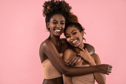 Excited emotional young women posing together , smiling and looking at camera. Pink pastel studio background. Beauty portrait of two afro female models. Perfect toothy smiles.