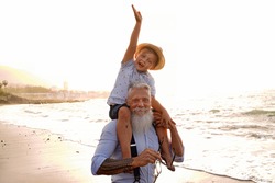 Little boy and senior man celebrating grandfather's day together, smiling, having fun on the beach. Real people emotions and family lifestyle concept. Summer time. 
            