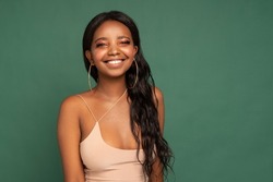 Adorable African young woman looks at the camera with joyful expression and big toothy smile. Beautiful dark skinned girl on green studio background. 