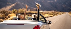 Dreams come true! Two happy young girls driving cabrio car during vacation road trip in mountains, making memories and having fun together. Back view.Freedom concept. Happiness. Tourist. 
