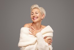 Beauty portrait of smiling adult blonde woman with short hairstyle and glamour makeup. Attractive lady wearing warm fashionable sweater. A lot of copy space. Studio shot.