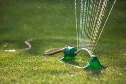 Lawn sprinkler spaying water over green grass. Irrigation system. backlight