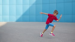 Cute little boy running over blue wall, urban scene